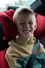 Charming baby without front tooth is sitting in the car and smiling