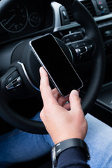 Closeup picture of male hands with smartphone driving a car