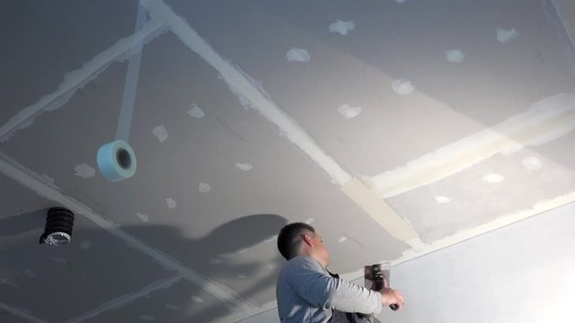 Handyman man spackling gypsum plasterboard ceiling with putty