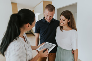 Estate agent using digital tablet showing young couple new house