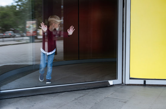 Boy Coming Out Of The Revolving Glass Doors Of A Store Leaning On Them