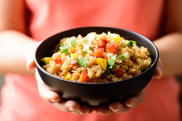 Hand holding bowl of fried rice with vegetables, Asian food	