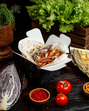 takeaway box with flatbread filled with chicken doner slices, cabbage, tomato, fries