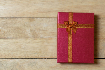 Red gift box with gold ribbon on wooden table background.