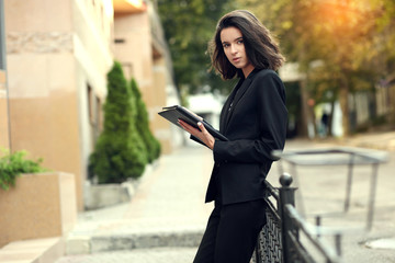 Fototapeta premium Beautiful brunette business woman in white suit with folder of documents in her hands outdoors. copy space