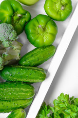 Fresh green vegetables - courgette, cucumber, paprika, parsley, broccoli on white tray and white background. Healthy snacks, vegetarian snacks concept. Organic vegetables concept