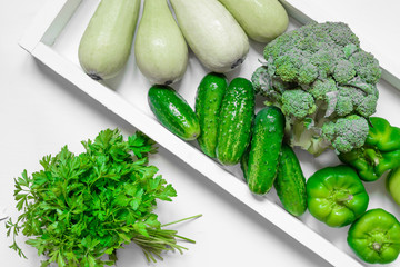 Fresh green vegetables - courgette, cucumber, paprika, parsley, broccoli on white tray and white background. Healthy snacks, vegetarian snacks concept. Organic vegetables concept