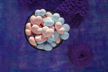 pink and blue meringue hearts on painted purple background with stripe and violet cotton mesh, and ball of cotton thread with copy space