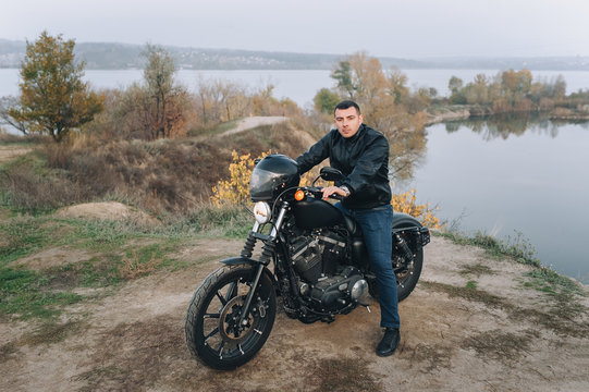 Stylish man in a black leather jacket sits on an expensive vintage motorcycle. Portrait of a brutal biker, gathered on a journey against the backdrop of nature in cloudy weather. Photography, concept.
