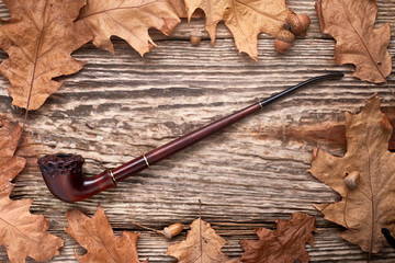 Tobacco pipe on old autumn wooden background.