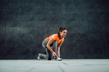 Fit attractive caucasian brunette in sportswear and with ponytail kneeling and tying shoelace before running.