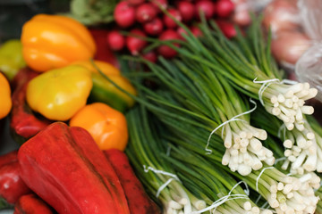 multi-colored vegetables on a market counter. Green onions, red and yellow peppers and tomatoes.