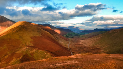 Obraz premium Scenic valley in autumn with snow capped mountain peaks. Touristic destination in the Lake District, Cumbria, United Kingdom. Top aerial view of peaks.