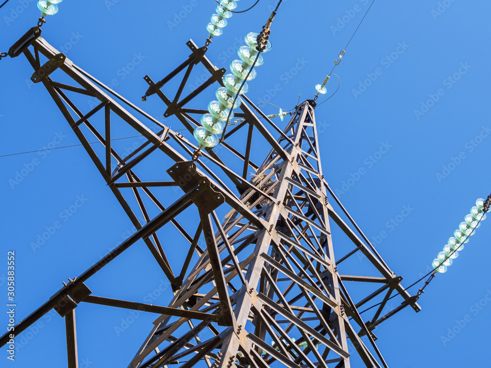 Wall mural metal pillars of power lines close up against the blue sky