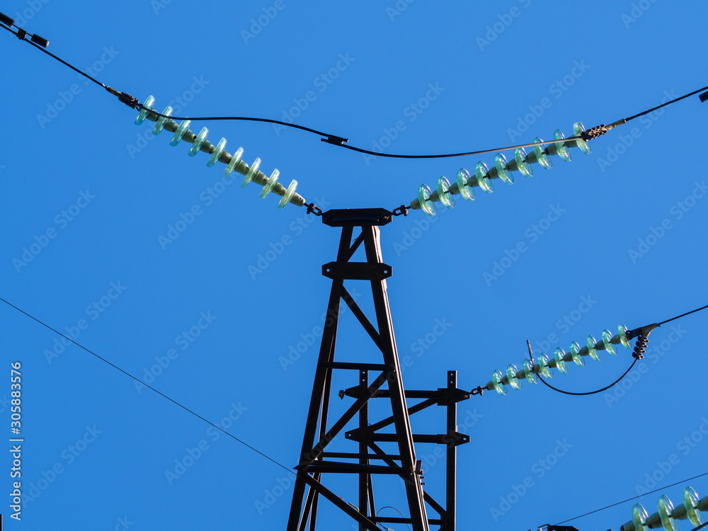 Wall mural metal pillars of power lines close up against the blue sky