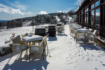 Terrace of a bar after a snowfall with tables and chairs completely covered with snow