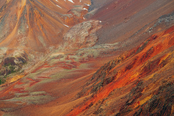 Vivid multicolor nature background of colorful highland valley among big rocky mountains. Full frame surface of giant red mountain rough wall and green valley. Green red orange yellow rocks.