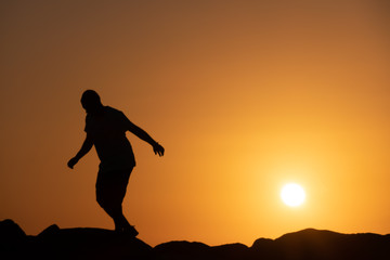 Man silhouette walking .on rocks, .orange sky at sunset.