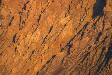 Sunny nature background of rockies in sunlight. Vivid natural mountain texture of big rough rocks. Full frame of bright giant craggy surface. Rocky mountain close-up. Plane of shiny rocks on sunset.