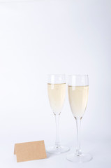 Vertical shot of two glasses of cgampagne and empty place card on the white background