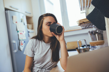 Fototapeta na wymiar young woman drinking coffee or tea in her kitchen