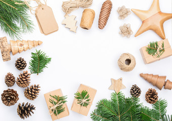 Fototapeta na wymiar Christmas frame background. Top view of fir tree branhes, brown gift boxes, various accessories for handmade presents, wooden decorations pinecones, tags on white table, copy space, selective focus