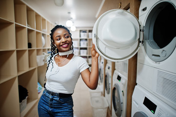Cheerful african american woman near washing machine in the self-service laundry.