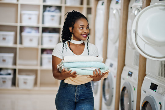 Cheerful african american woman with towels in hands near washing machine in the self-service laundry.