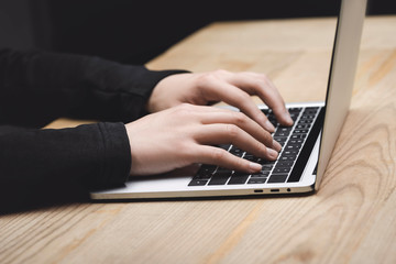 cropped view of hacker using laptop and sitting at table