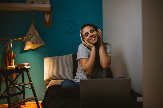 young woman student sitting on bed in her room using laptop computer