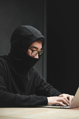 asian hacker with obscured face using laptop and sitting at table