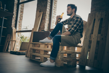 Low below angle view photo of serious pensive man holding bottle of alcohol beverage sitting on...