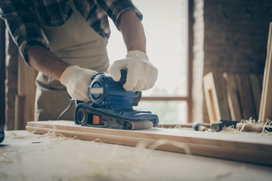 Cropped close up photo of man working with sandpaper surrounded with filings processing wooden block with hands in gloves