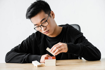 asian seo manager playing with wooden rectangles with lettering seo