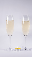 Burning candle near glasses of champagne, on a white background