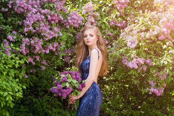 Obraz na płótnie Canvas Portrait of young beautiful blonde woman posing among blooming lilac. Outdoor fashion photo of young woman surrounded by flowers. Spring blossom