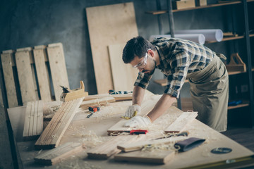 Profile side view portrait of his he nice attractive focused skilled experienced hardworking guy self-employed builder carving wood on table desk at modern industrial loft brick style interior indoors