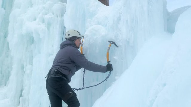 Alpinist man with ice tools axe climbing a large wall of ice