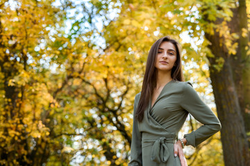 Fototapeta na wymiar Portrait of brunette woman in green dress posing in autumn park