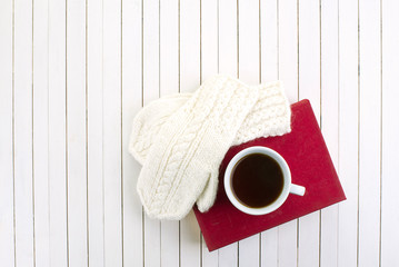 Red book and white cup of coffee on the white wooden background with autumn, winter accesories. Leisure time with book, drinking coffe