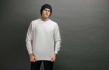 Man wearing white sweatshirt and a black hat standing over gray background. Sweatshirt or hoodie...