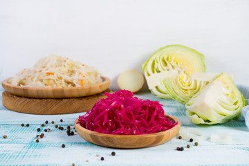 Different colors fermented cabbage lies in wooden plates and around fresh vegetables.