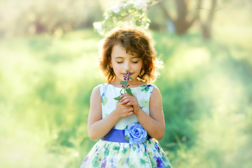 Fototapeta premium Little girl with closed eyes in the garden with violet flower in hands. Allergic in springtime. Natural light.