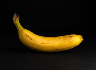 Ripe banana isolated on black background. Dark food photography with copy space.