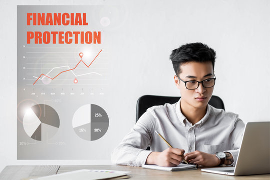 asian seo manager using laptop and sitting near illustration with financial protection lettering