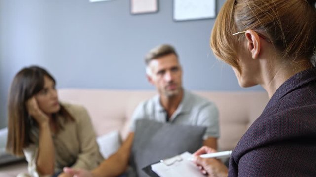 Irritated couple man and woman having a conversation with a psychologist on therapy session in room