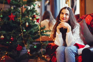 Pretty girl sitting near Christmas tree. Beautiful lady in a studio