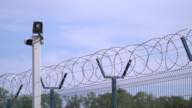 Modern prison fence and a pole with cameras on it, barbed wire