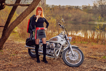 Fototapeta na wymiar red-haired female biker next to a tourist motorcycle at sunset