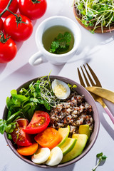 Vegetarian breakfast with quinoa, eggs, microgreen and vegetables, green tea with mint on a white table, flat lay